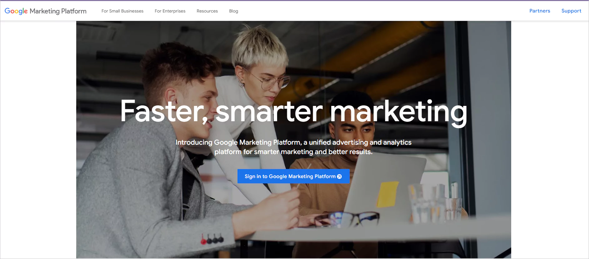 Three diverse professionals collaborate around laptop in modern office, overlay text reads 'Faster, smarter marketing'.